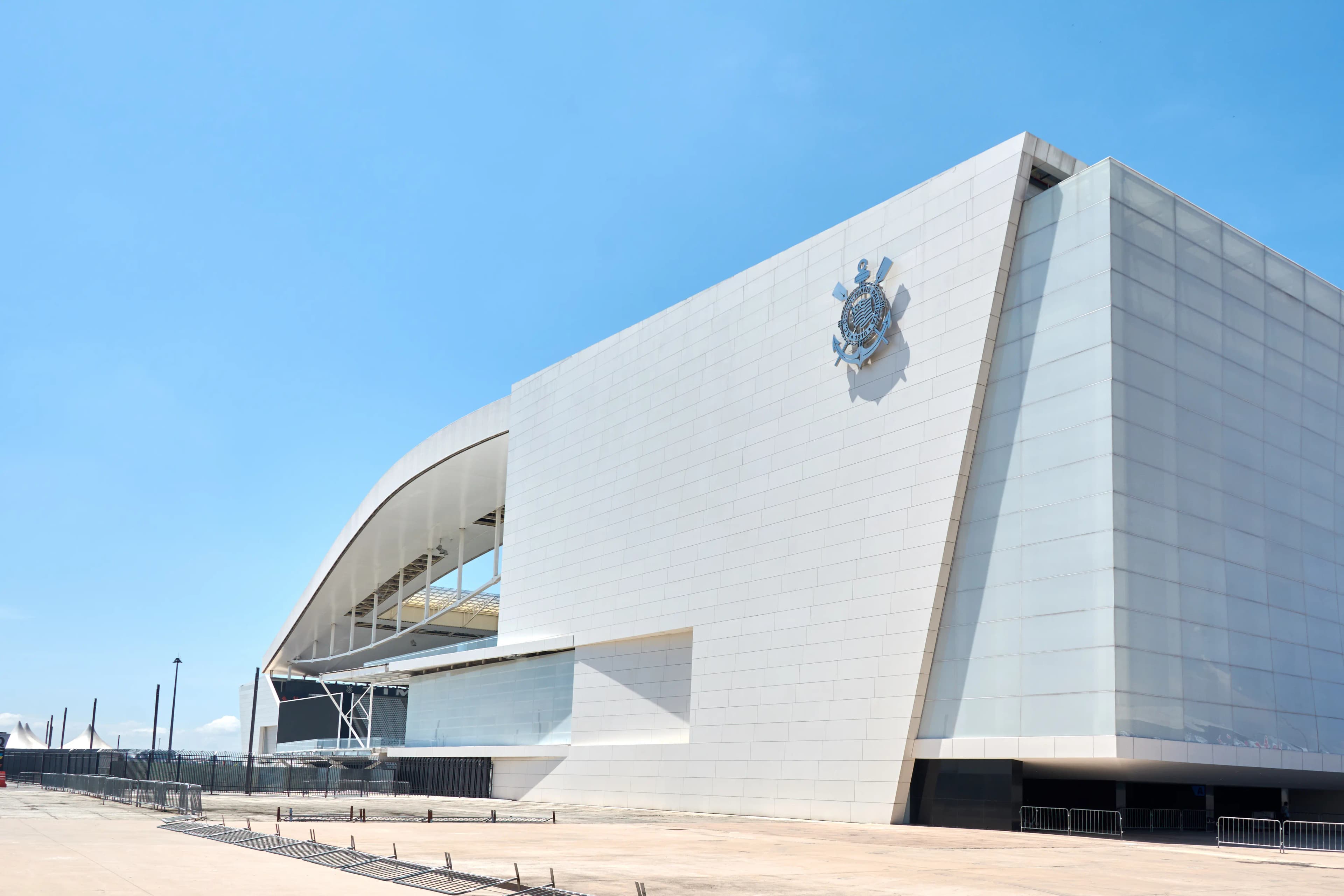 Vista da fachada da Neo Química Arena, estádio do Corinthians, com céu azul.