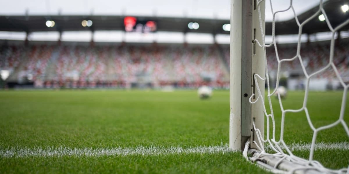 Imagem widescreen de um campo de futebol com foco na trave e na rede do gol, enquanto a arquibancada aparece desfocada ao fundo, representando quantos gols jogadores do Corinthians fizeram em Copas do Mundo em contexto de grandes competições internacionais.