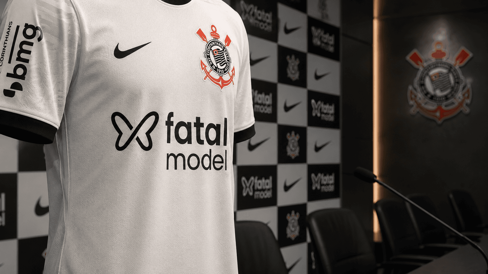 Camisa branca do Corinthians com o patrocínio Fatal Model em destaque, fotografada em ambiente institucional de coletiva de imprensa, com painel do clube e cadeiras ao fundo, em composição séria e profissional.